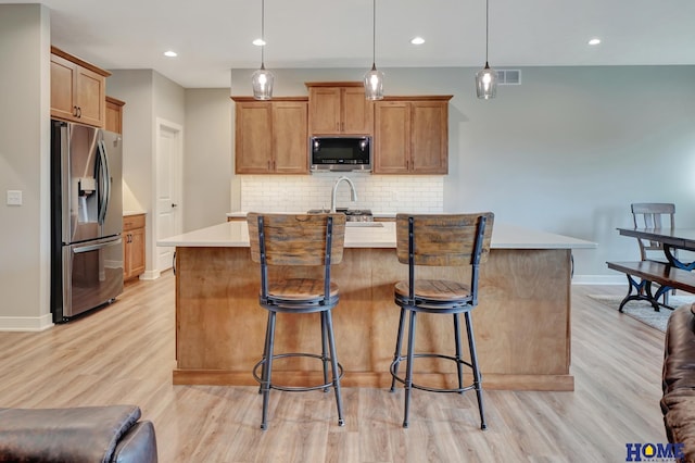 kitchen with stainless steel appliances, hanging light fixtures, an island with sink, and light countertops