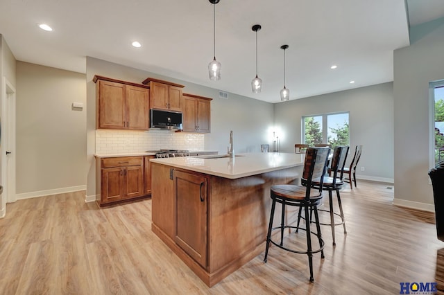 kitchen featuring a center island with sink, brown cabinetry, decorative light fixtures, light countertops, and a sink