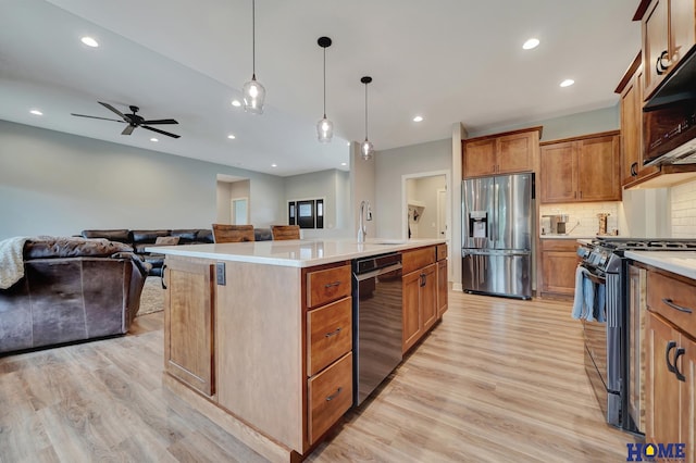 kitchen with a center island with sink, light countertops, hanging light fixtures, appliances with stainless steel finishes, and open floor plan