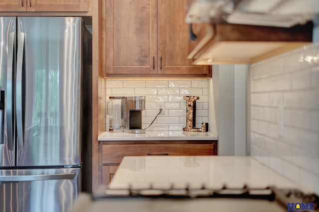 kitchen featuring brown cabinets, stainless steel fridge, light countertops, and decorative backsplash