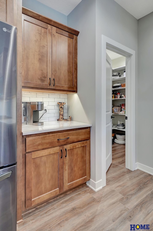 kitchen featuring light wood-type flooring, tasteful backsplash, light countertops, and freestanding refrigerator