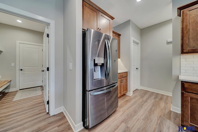 kitchen with light wood-type flooring, light countertops, stainless steel fridge, and backsplash