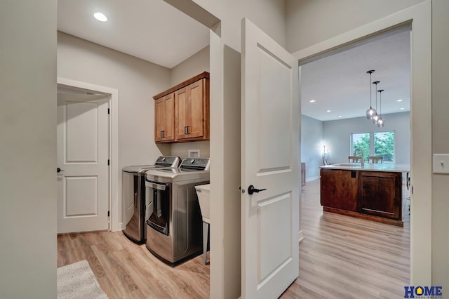 washroom with cabinet space, light wood-type flooring, washing machine and dryer, a sink, and recessed lighting