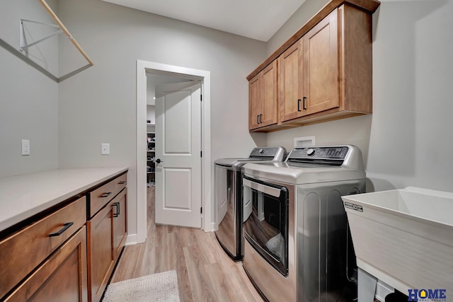 laundry area with cabinet space, light wood-style floors, separate washer and dryer, and a sink