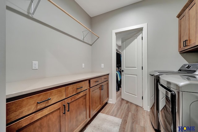 laundry area with washing machine and clothes dryer, cabinet space, and light wood-style floors