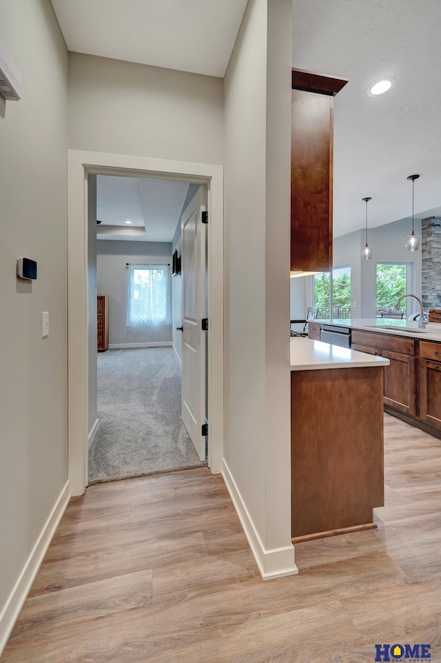 hall with light wood-style flooring, baseboards, a sink, and recessed lighting