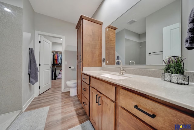 full bathroom with visible vents, toilet, wood finished floors, a walk in closet, and vanity