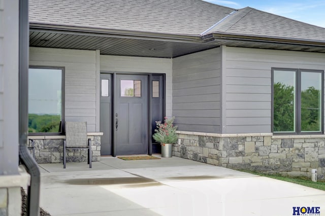 view of exterior entry with stone siding and roof with shingles