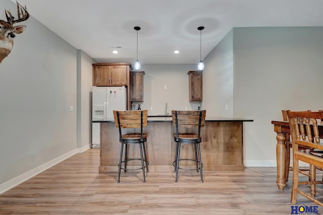 kitchen featuring brown cabinetry, light wood-style flooring, a breakfast bar, and decorative light fixtures