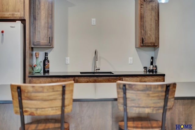 kitchen with dark countertops, brown cabinets, a sink, and freestanding refrigerator