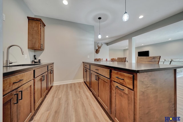 kitchen featuring dark countertops, hanging light fixtures, brown cabinetry, a sink, and a peninsula