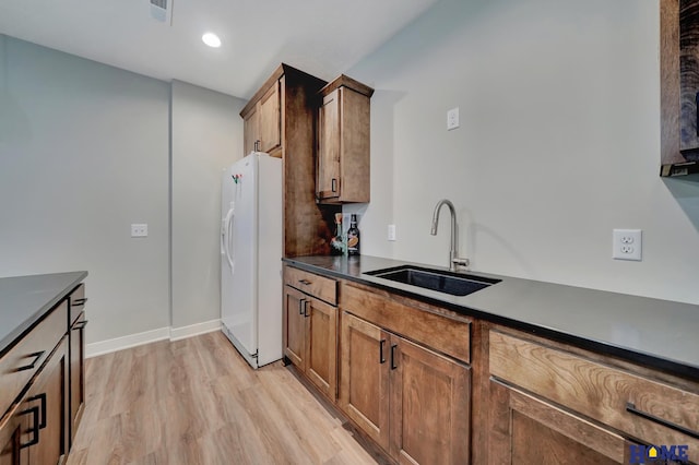 kitchen with white refrigerator with ice dispenser, visible vents, light wood-style flooring, brown cabinets, and a sink