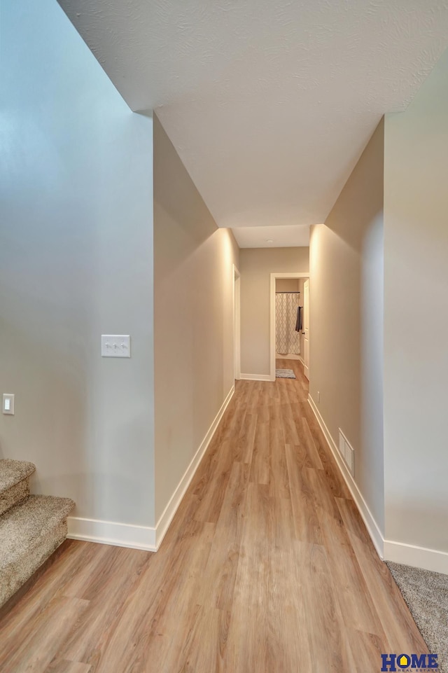 corridor with light wood finished floors, baseboards, stairway, and visible vents