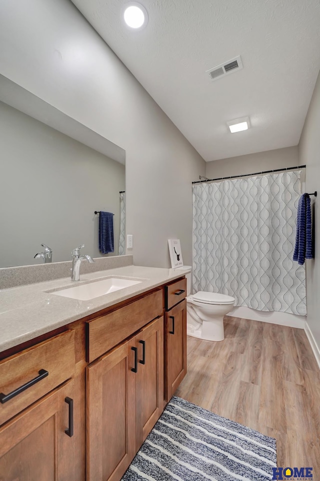 full bath featuring a textured ceiling, toilet, wood finished floors, vanity, and visible vents