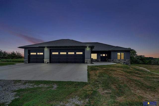 prairie-style home with a garage, stone siding, driveway, and a front lawn