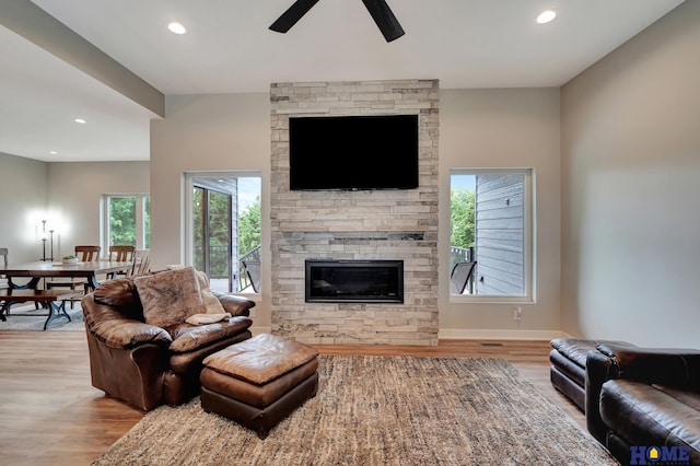 living area with baseboards, a ceiling fan, light wood-style flooring, a stone fireplace, and recessed lighting