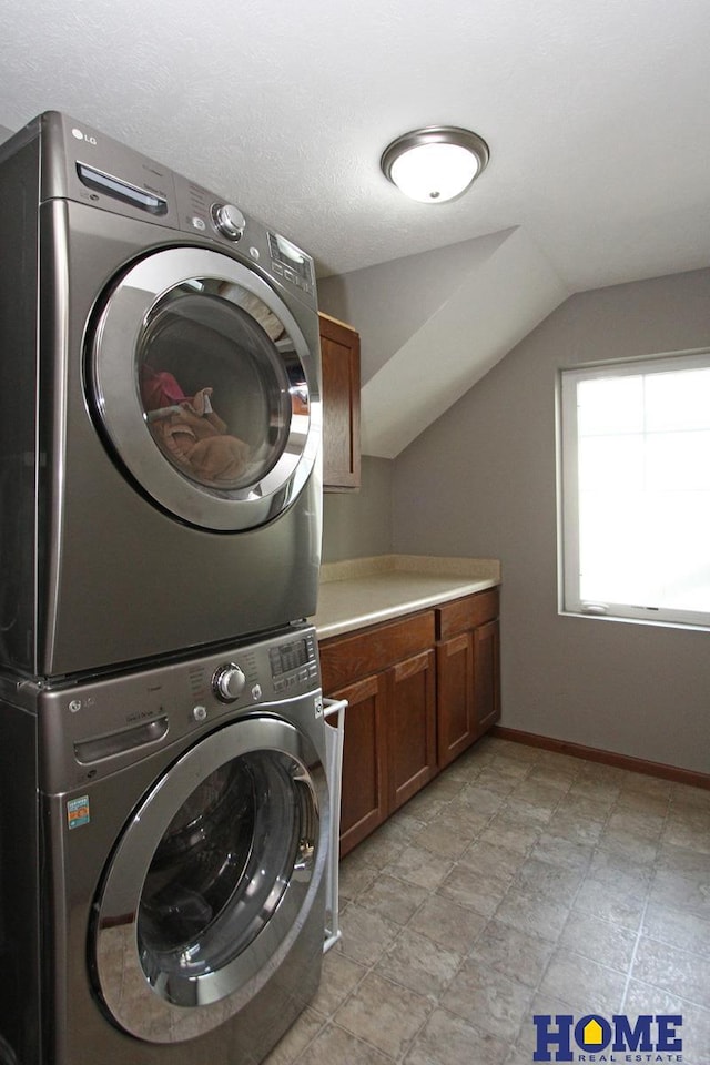 clothes washing area featuring cabinet space, stacked washer and clothes dryer, and baseboards