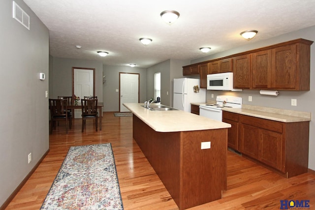 kitchen featuring white appliances, a center island with sink, visible vents, light countertops, and a sink