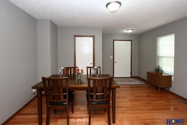 dining space featuring light wood-style flooring, baseboards, and a textured ceiling