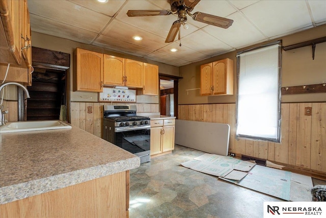 kitchen featuring stainless steel gas stove, wooden walls, wainscoting, light countertops, and a sink