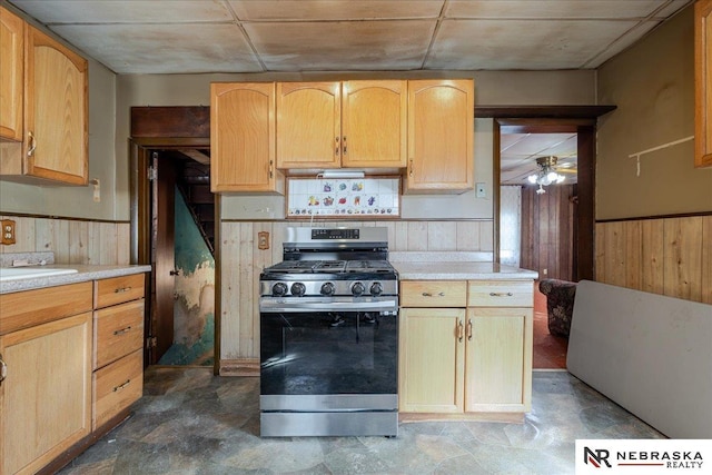 kitchen with stainless steel gas range, a wainscoted wall, light countertops, and wood walls