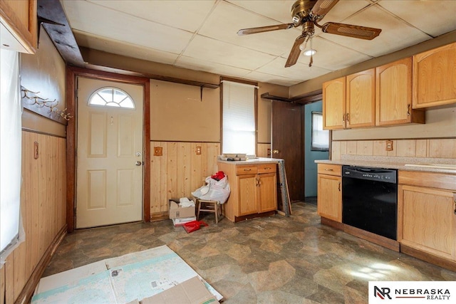 kitchen featuring wooden walls, black dishwasher, light countertops, wainscoting, and stone finish flooring