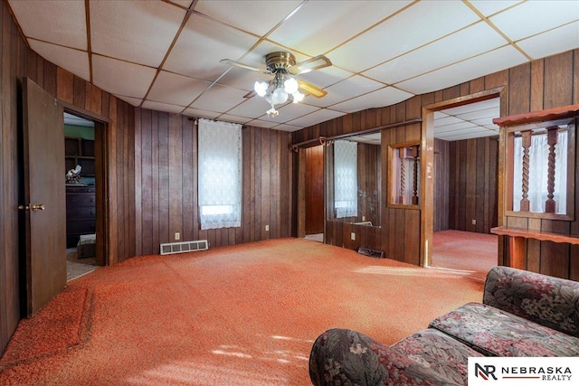 living room featuring a paneled ceiling, wood walls, carpet, and visible vents