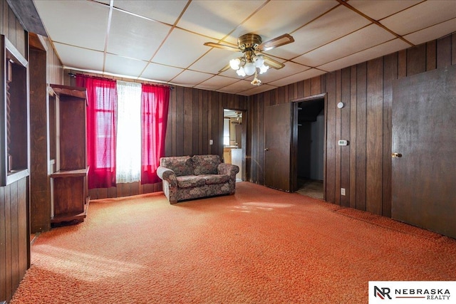 unfurnished room featuring carpet, wooden walls, a drop ceiling, and a ceiling fan