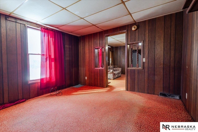 spare room featuring a drop ceiling, carpet flooring, visible vents, and wooden walls