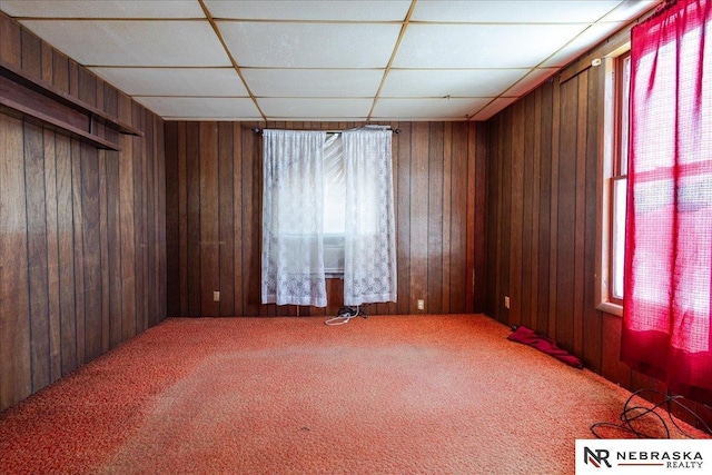 unfurnished room with carpet floors, a drop ceiling, and wooden walls