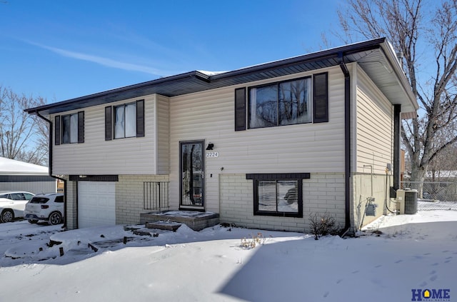 raised ranch with a garage, central AC unit, and brick siding