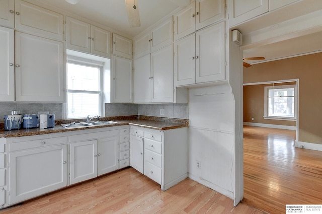 kitchen featuring light wood finished floors, plenty of natural light, a sink, and white cabinets