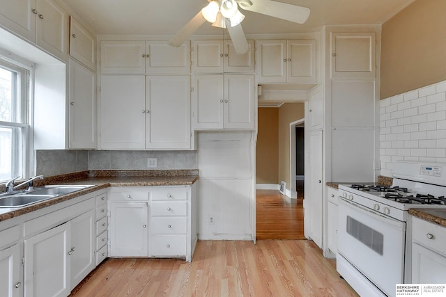 kitchen with dark countertops, white gas range oven, a sink, and white cabinets