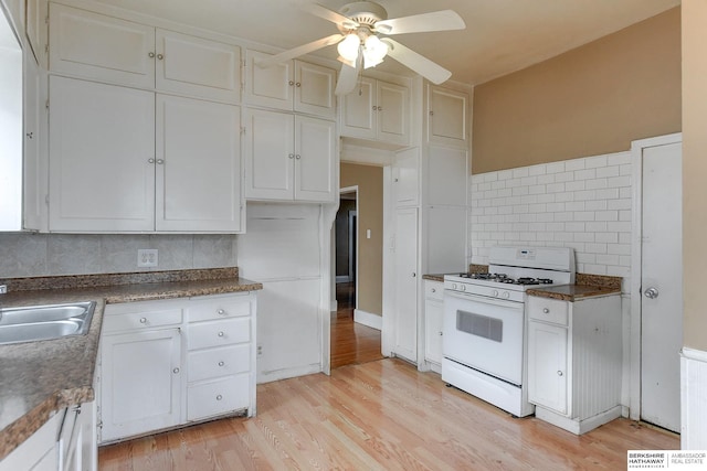 kitchen featuring dark countertops, backsplash, white cabinets, light wood-type flooring, and white range with gas stovetop