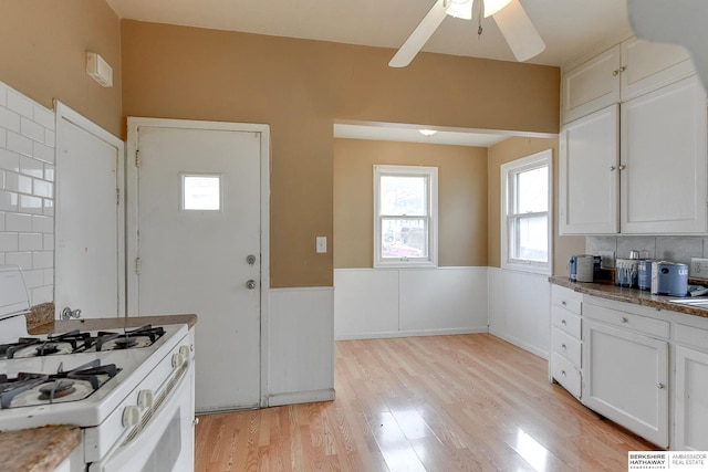 kitchen with ceiling fan, light wood-style flooring, white cabinetry, wainscoting, and white gas range oven