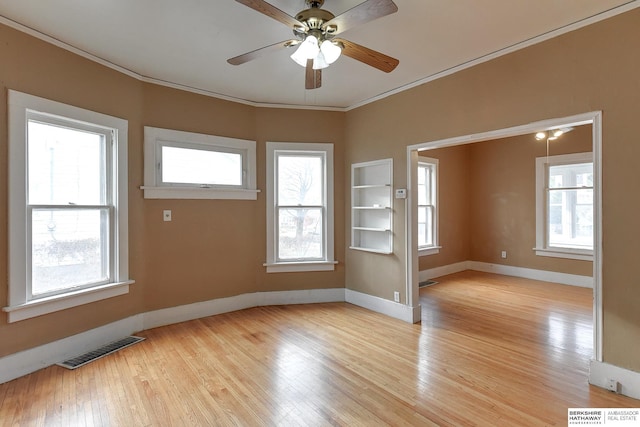 empty room with ornamental molding, a wealth of natural light, visible vents, and light wood finished floors