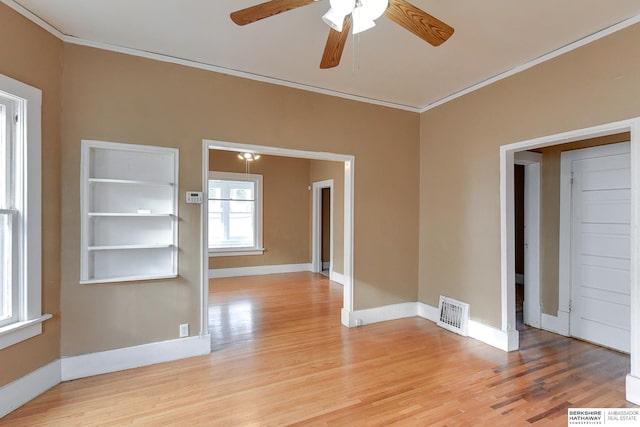 spare room featuring a ceiling fan, visible vents, baseboards, ornamental molding, and light wood-type flooring