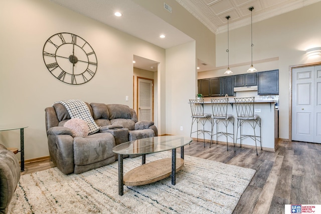 living room featuring baseboards, visible vents, a towering ceiling, wood finished floors, and recessed lighting