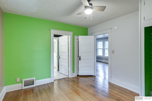 spare room with visible vents, light wood-style floors, a ceiling fan, a textured ceiling, and baseboards