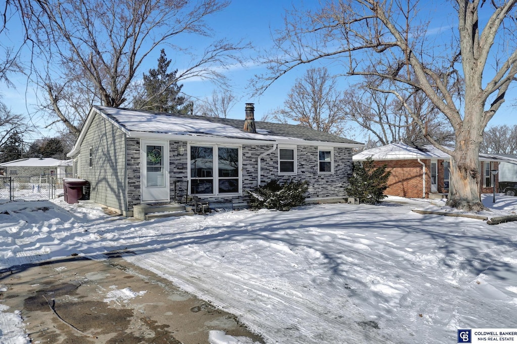 view of front of property featuring entry steps, stone siding, fence, and a chimney