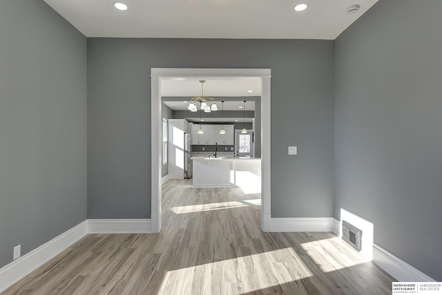 unfurnished dining area featuring light wood finished floors, a sink, visible vents, and baseboards