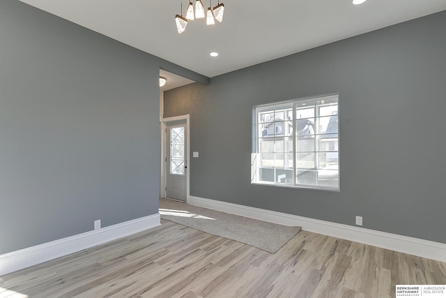 empty room with a notable chandelier, recessed lighting, light wood-type flooring, and baseboards