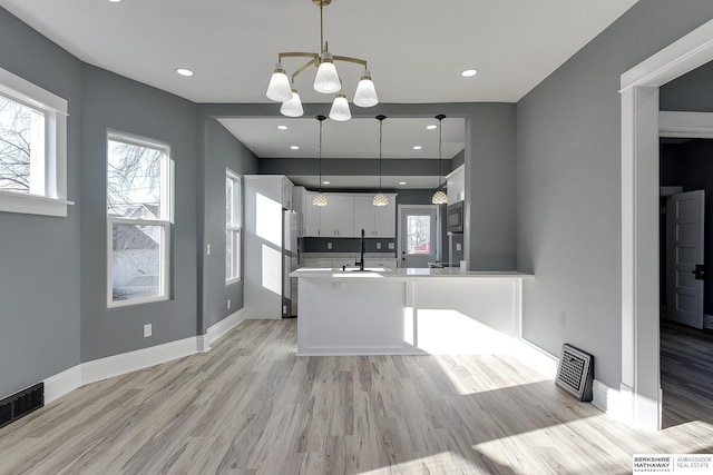 kitchen with white cabinets, a peninsula, light countertops, black microwave, and pendant lighting