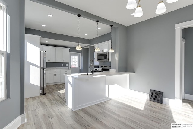 kitchen featuring stainless steel appliances, a peninsula, white cabinetry, light countertops, and decorative light fixtures