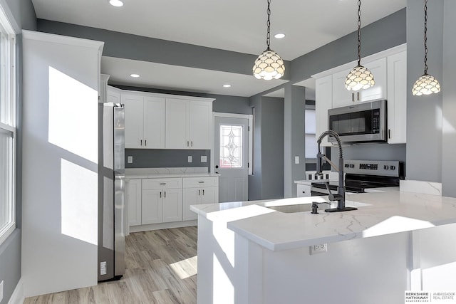 kitchen with stainless steel appliances, pendant lighting, white cabinetry, and light stone countertops