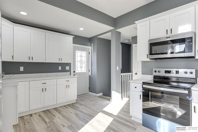 kitchen with light wood-style flooring, white cabinetry, baseboards, appliances with stainless steel finishes, and light stone countertops