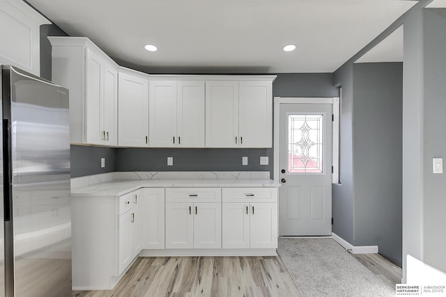 kitchen with light stone counters, light wood-style floors, freestanding refrigerator, and white cabinetry