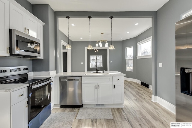 kitchen with stainless steel appliances, pendant lighting, light countertops, and white cabinetry