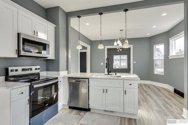 kitchen with stainless steel appliances, white cabinetry, a sink, and decorative light fixtures