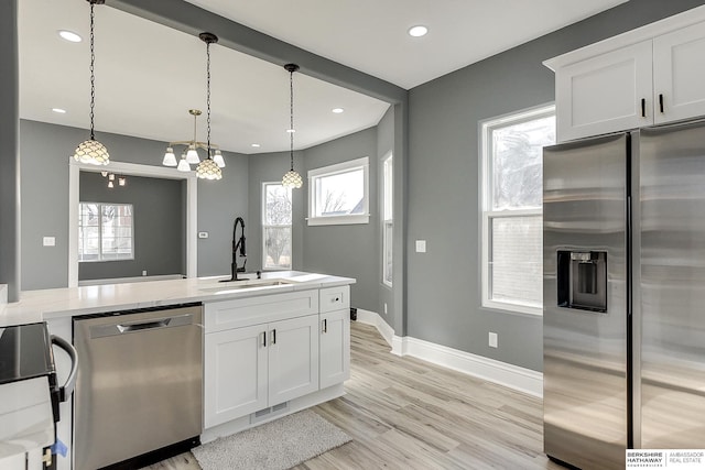 kitchen with white cabinets, light wood-style flooring, hanging light fixtures, stainless steel appliances, and a sink